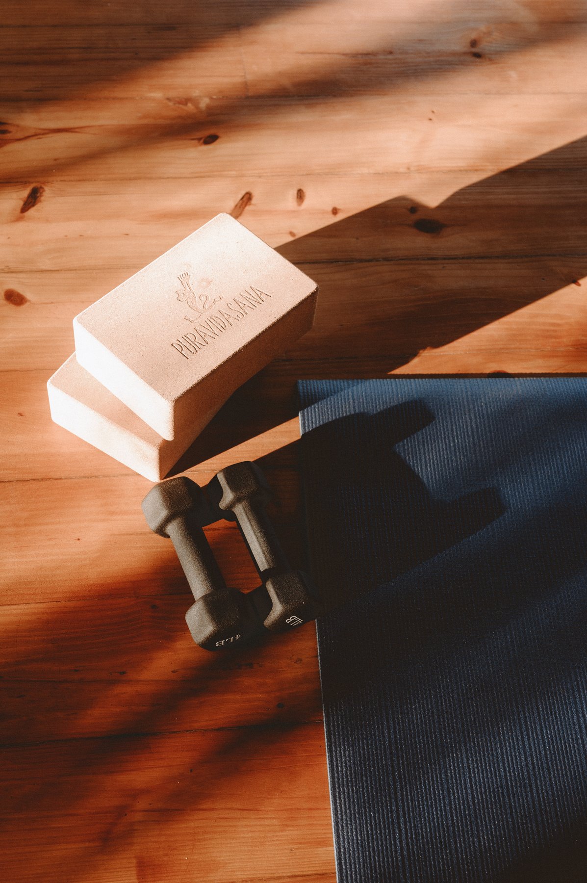 Yoga blocks, dumbbells, and a mat laid out on the studio's wood floor
