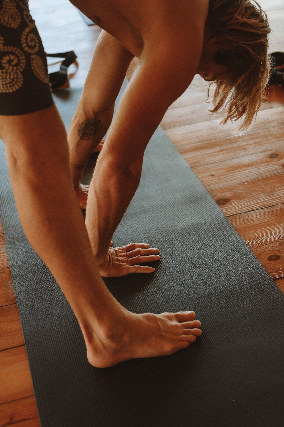 A BodyKult instructor giving a student a hands-on assist during a forward fold stretch